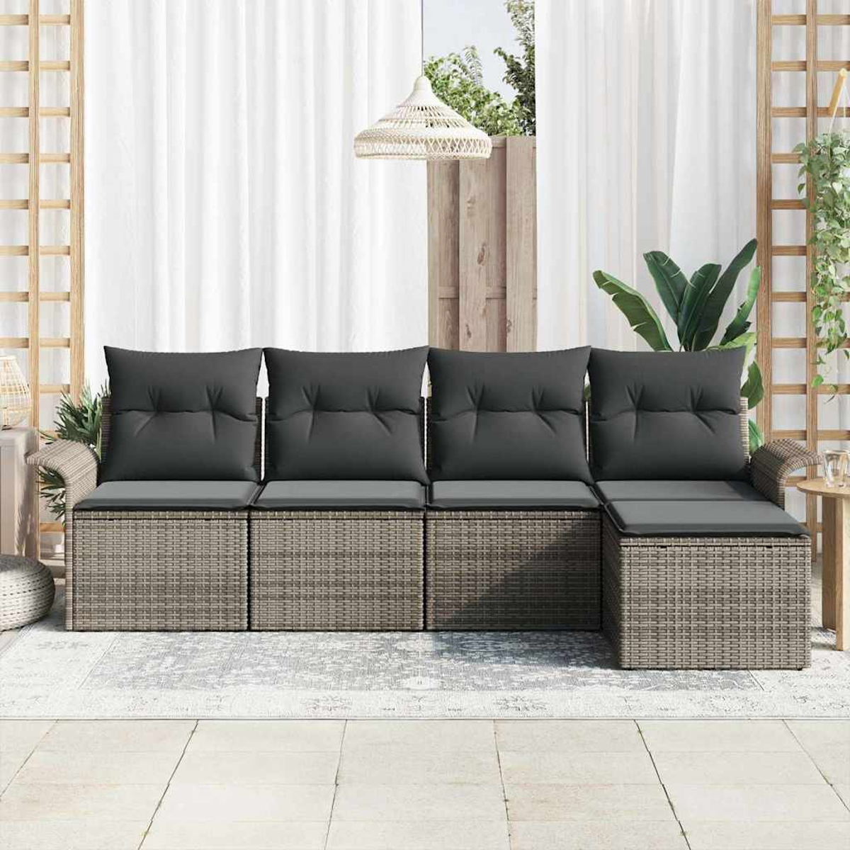 Graues Rattansofa mit dunkelgrauen Kissen auf der Terrasse. Weiße Vorhänge und Pflanzen im Hintergrund.