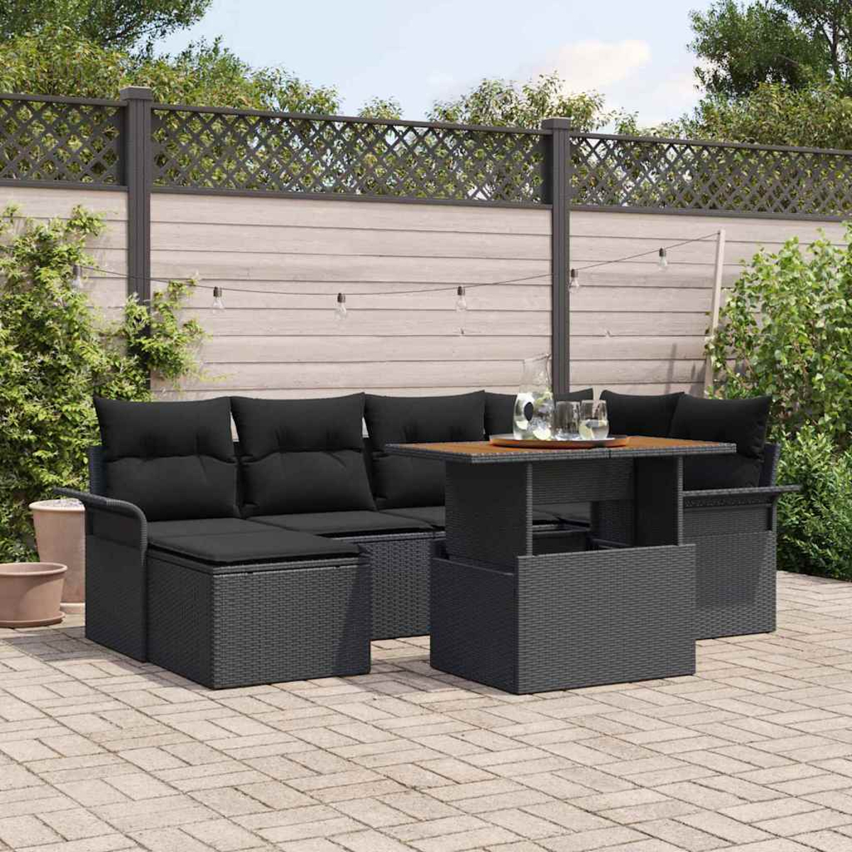 Garten-Set mit schwarzen Kissen, Tisch und Sitzgelegenheiten. Hintergrund: Zaun, Grün und Backstein-Patio.