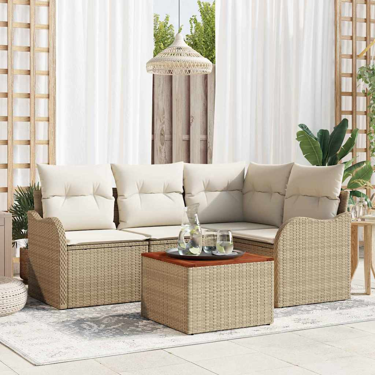 Outdoor-Korbsessel mit cremefarbenen Kissen, Couchtisch mit Getränken und Hängelampe. Weiße Vorhänge und Grün im Hintergrund.