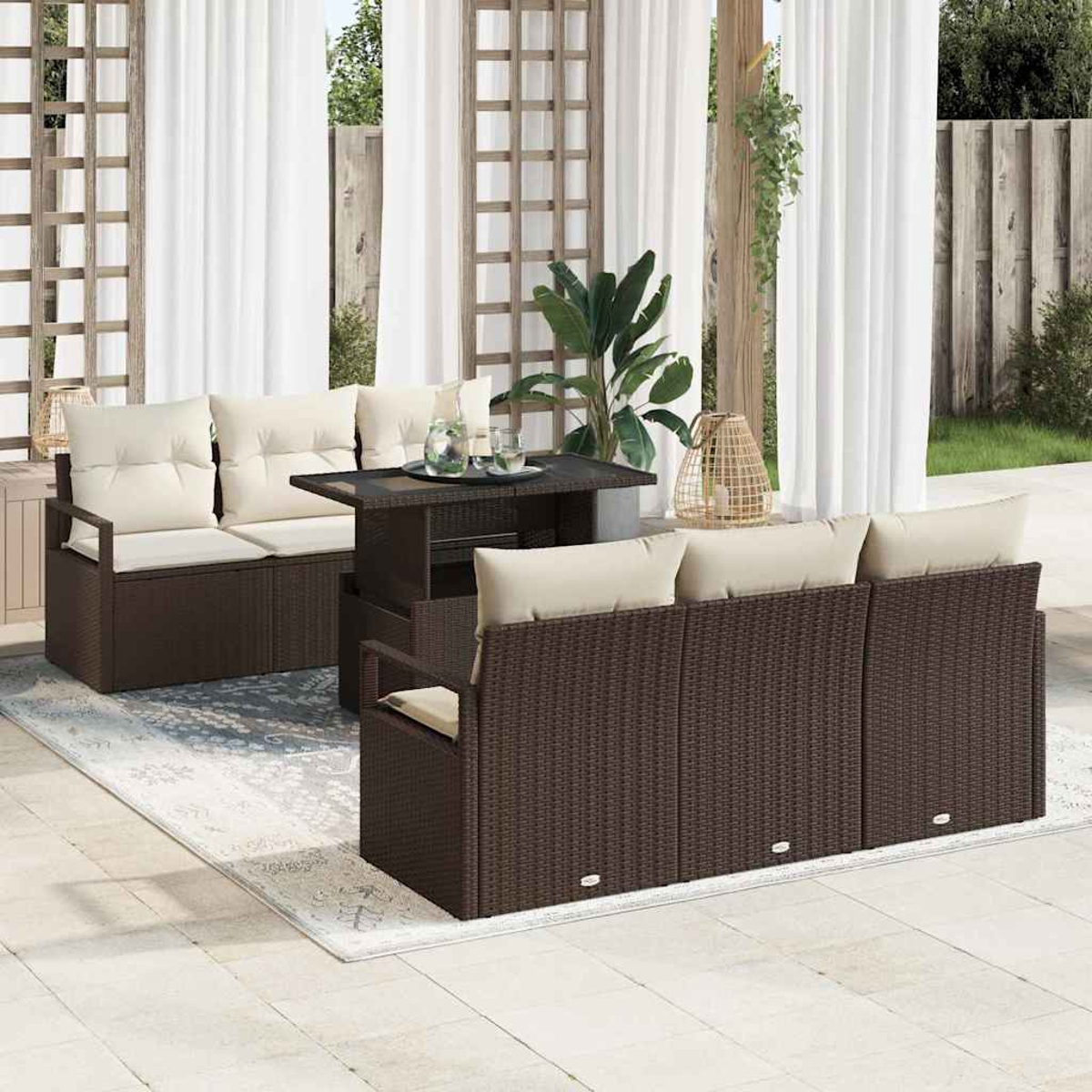 Terrassenset: braunes Korbmöbel-Sofa, Tisch und Bank mit cremefarbenen Kissen. Weiße Vorhänge und Pflanzen im Hintergrund.