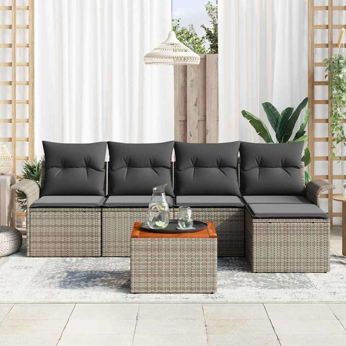Outdoor-Korbsessel mit grauen Kissen, Couchtisch mit Getränken und weißen Vorhängen im Hintergrund.
