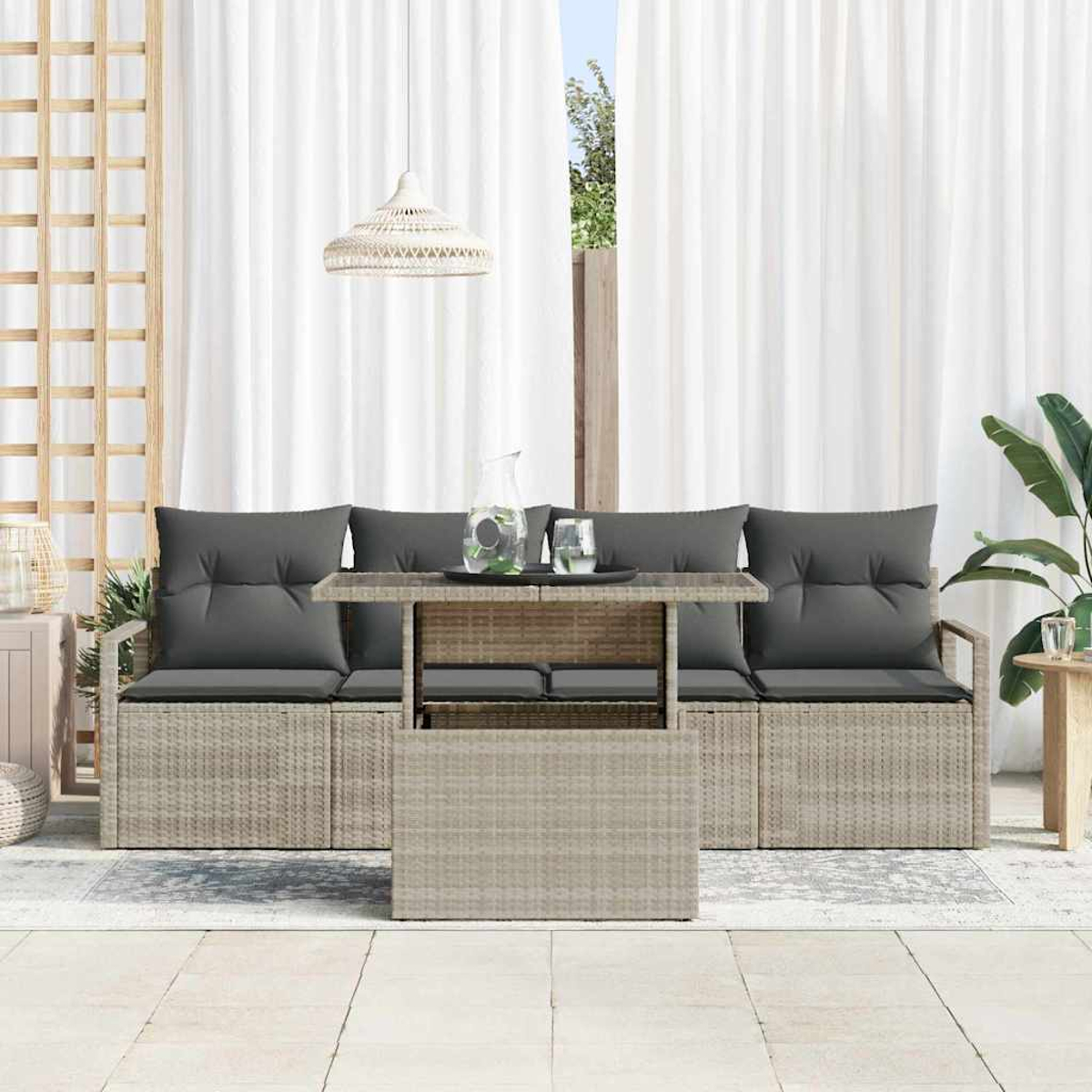 Juego de patio al aire libre con cojines grises, una mesa con bebidas y cortinas blancas. Una lámpara cuelga arriba. Hay plantas y detalles en madera.