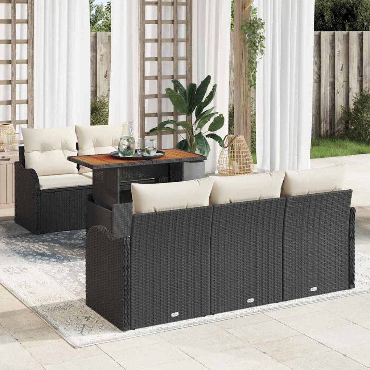 Terrassenmöbel-Set mit dunklen Korbmöbeln und cremefarbenen Kissen. Ein Holztisch mit Getränken und Dekoleuchte.
