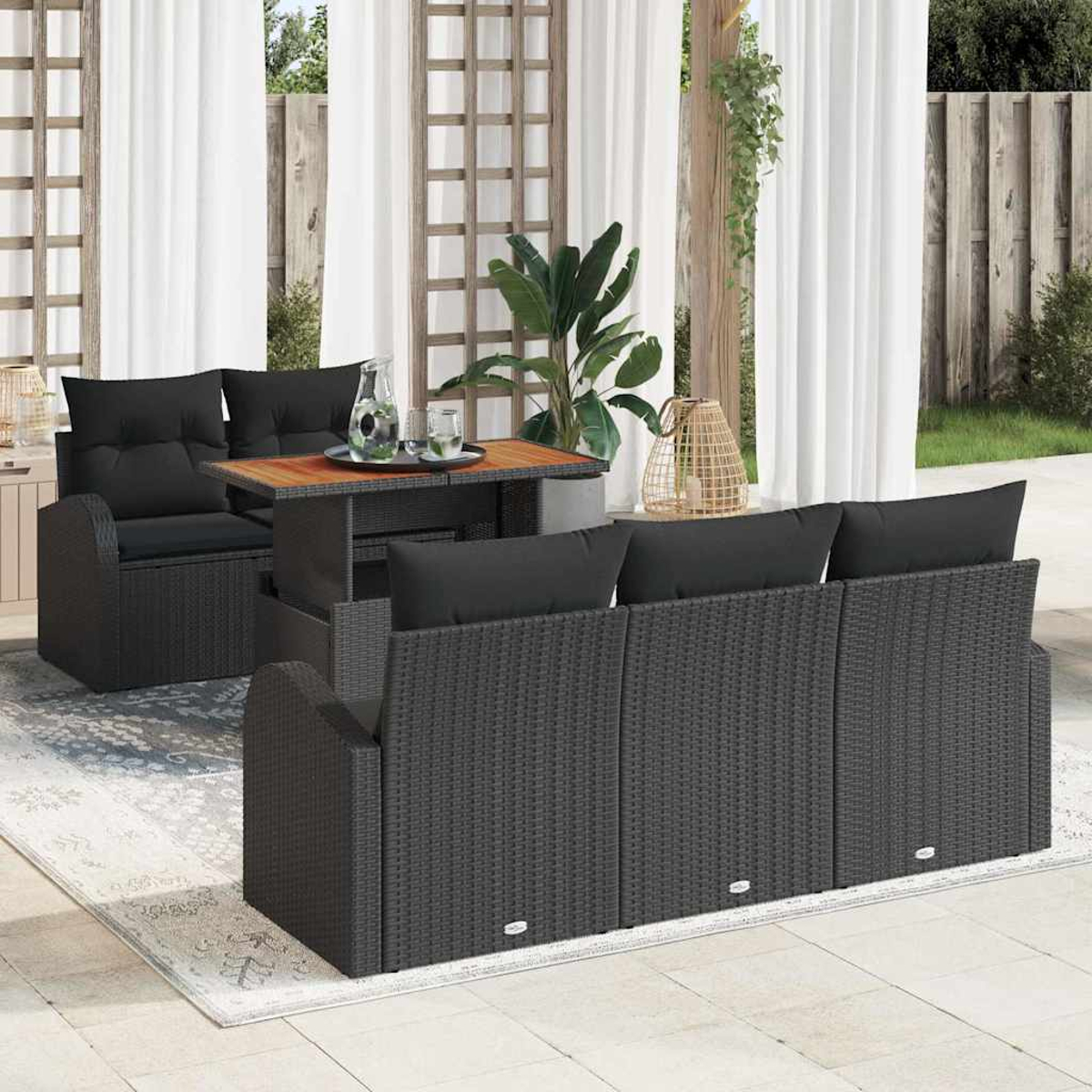 Terrassenset mit schwarzem Korbmöbeln, Tisch mit Getränken und einem Teppich. Weiße Vorhänge und Pflanzen im Hintergrund.