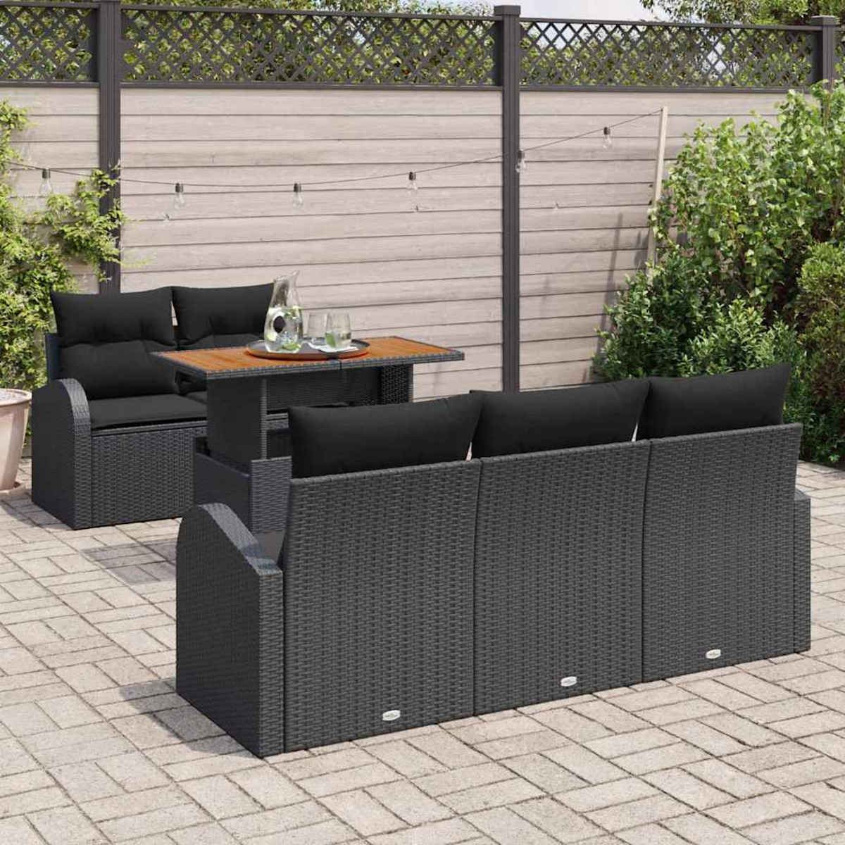 Garten-Terrassenset mit schwarzen Kissen. Ein Tisch mit Getränken steht zwischen einer Couch und einem Dreisitzer. Im Hintergrund ist ein Zaun zu sehen.