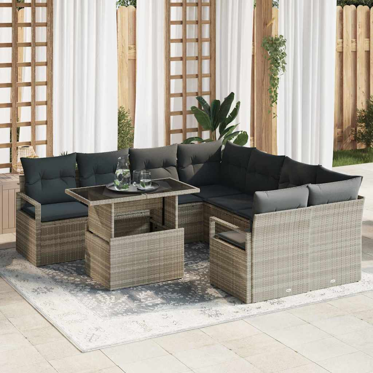 Gartenmöbel-Set aus Korbgeflecht mit dunklen Kissen. Inklusive Tisch mit Gläsern und einer Wasserkaraffe, auf einem gemusterten Teppich.