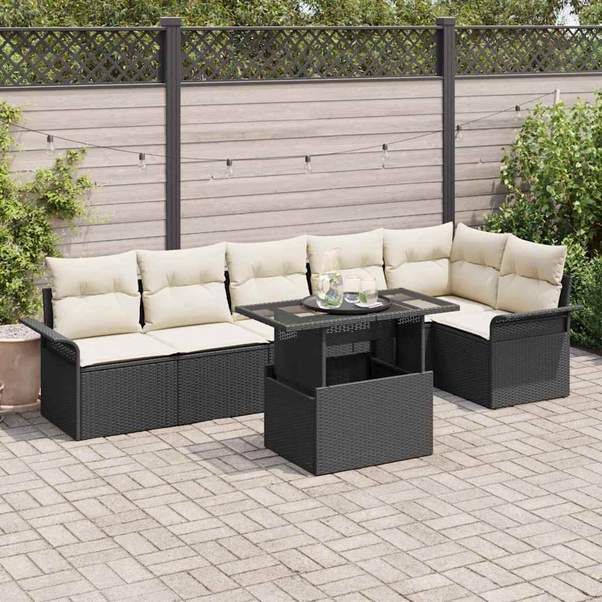 Terrassenmöbel-Set mit schwarzem Korbmöbeln und beigefarbenen Kissen. Enthält einen Tisch mit Gläsern und Lichterketten im Hintergrund.