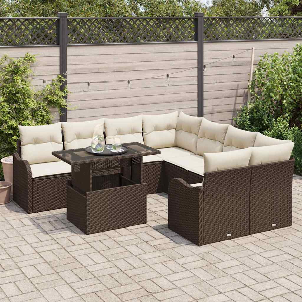 Gartenmöbel-Set aus Korbgeflecht mit beigen Kissen, einem Tisch mit Gläsern und einem Zaun im Hintergrund.