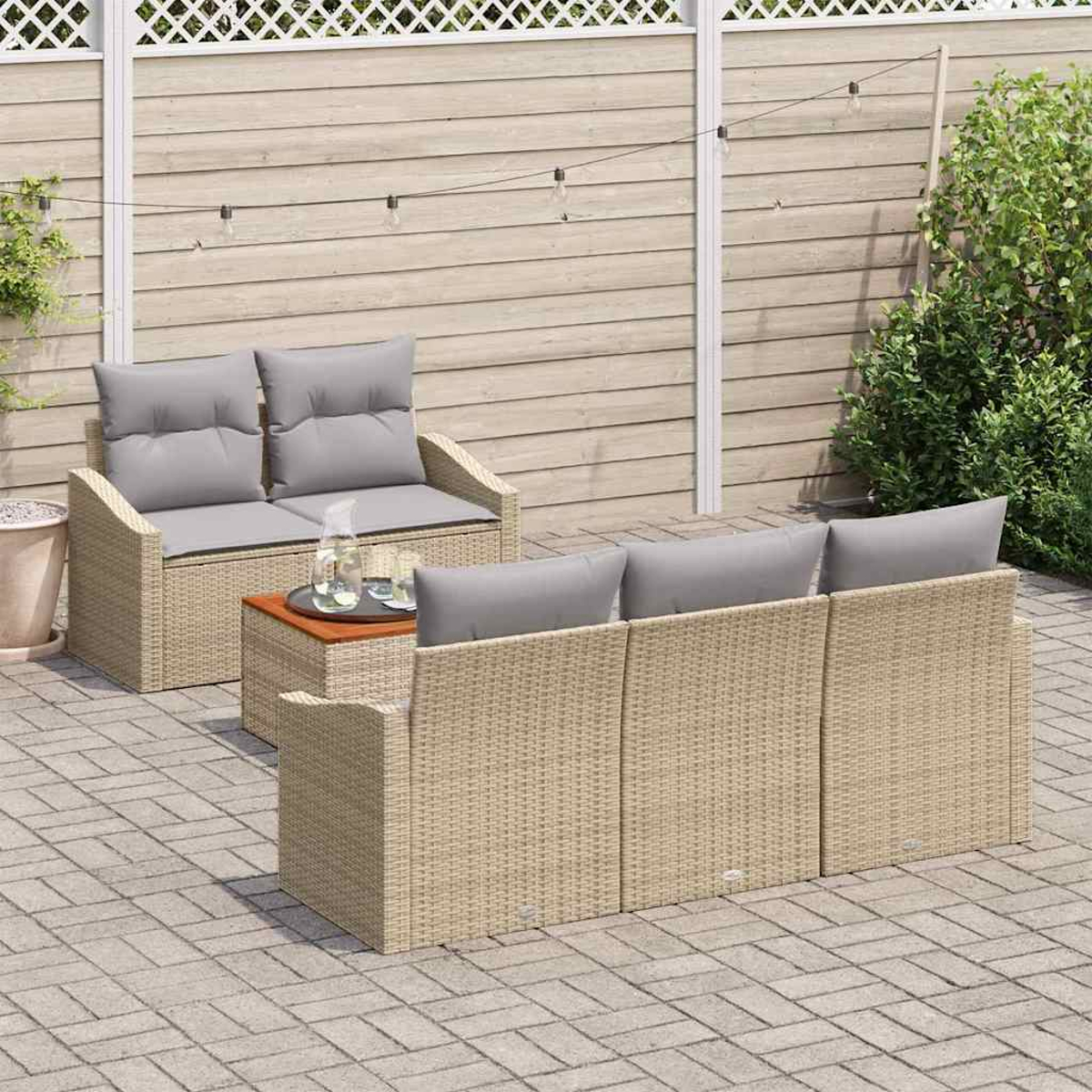 Gartenmöbel-Set aus Korbgeflecht mit grauen Kissen. Beinhaltet ein Sofa, einen Zweisitzer und einen kleinen Tisch auf einer Ziegelterrasse. Im Hintergrund ein Zaun.