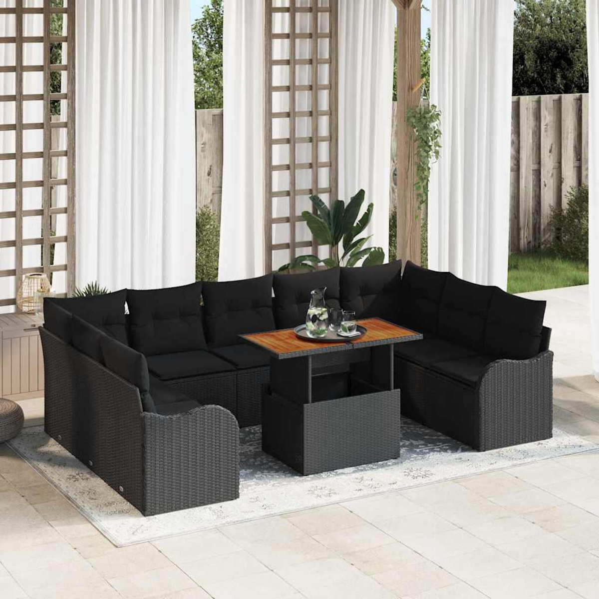 Garten-Lounge-Set mit schwarzen Kissen auf grauem Korbmöbel. Ein Tisch mit Getränken steht in der Mitte. Weiße Vorhänge im Hintergrund.