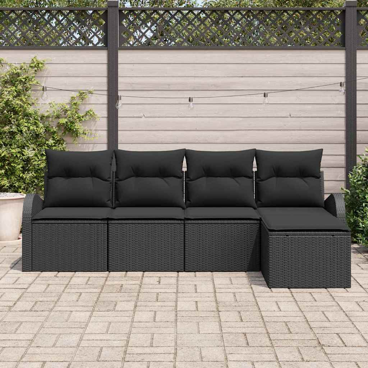 Schwarzes Outdoor-Sofa aus Korbgeflecht mit schwarzen Kissen. Es steht auf einer Steinterrasse vor einem Holzzaun.