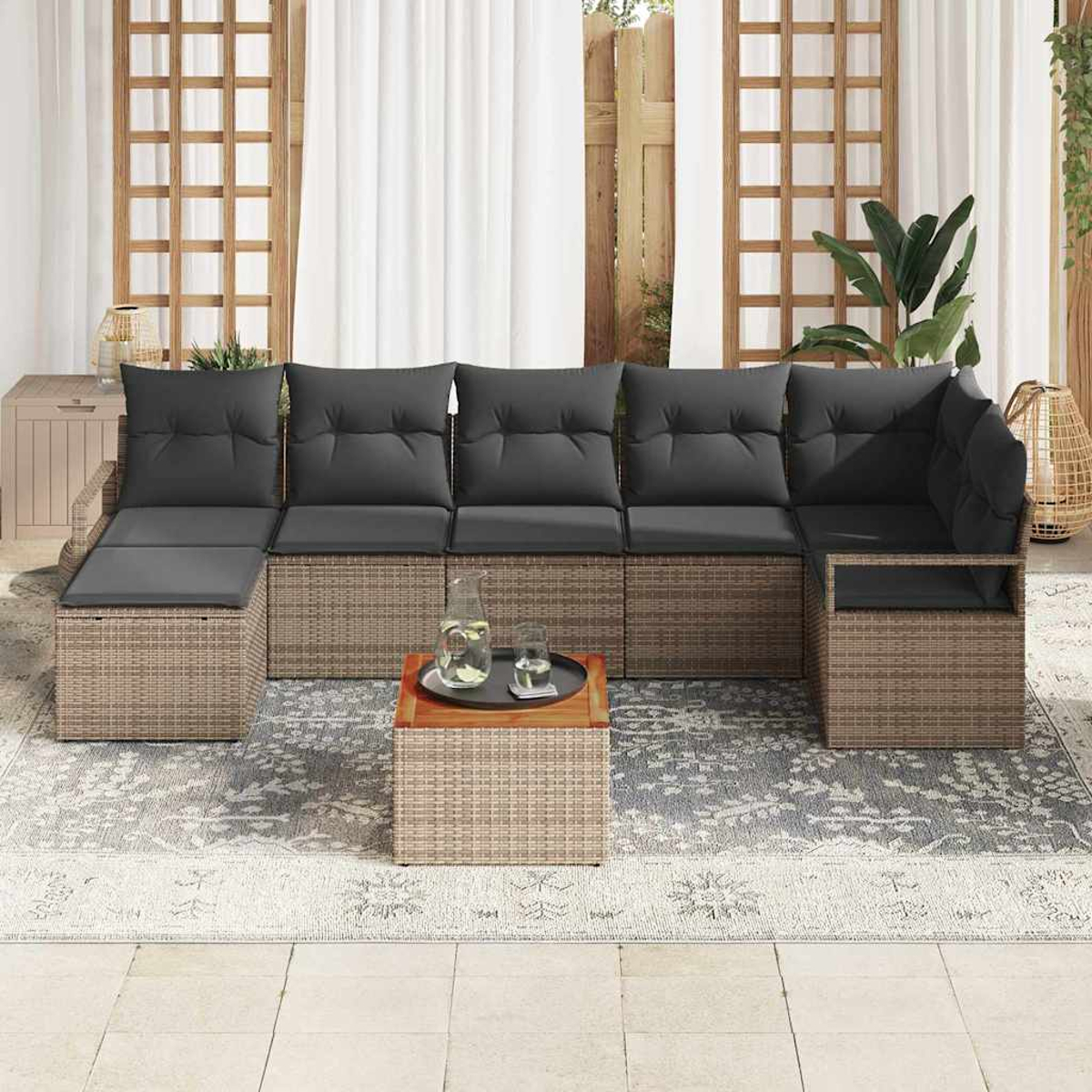 Ein Rattansofa mit grauen Kissen steht auf einem gemusterten Teppich. Ein Holztisch trägt ein Tablett mit Wasser und Gläsern.