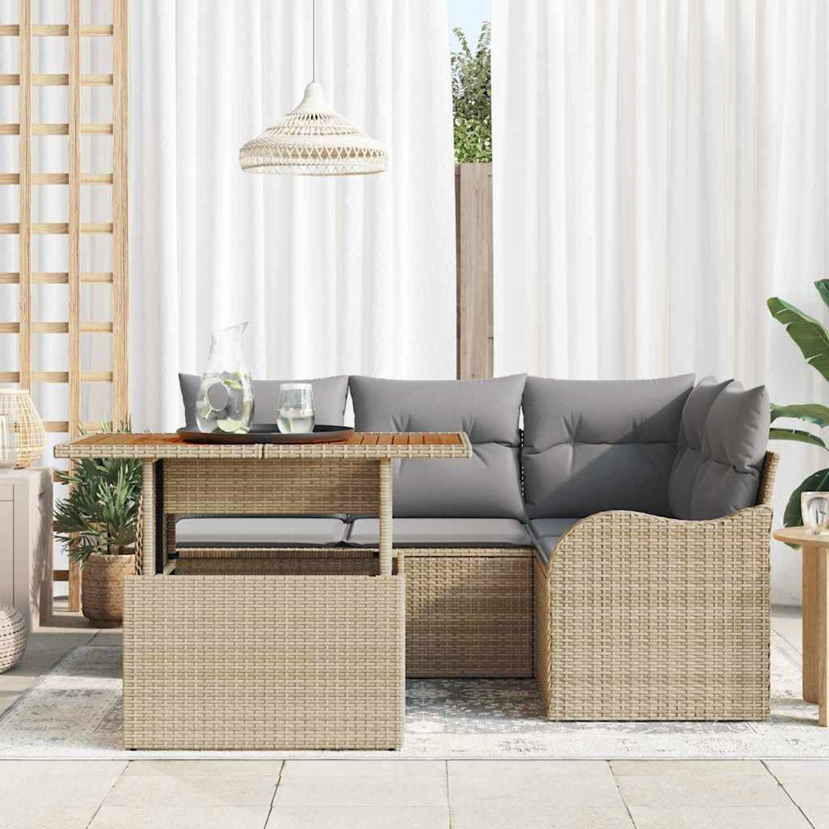 Geflochtenes Outdoor-Möbelset mit Tisch und Sofa mit grauen Kissen. Eine Glaskanne und Vorhänge sind im Hintergrund zu sehen.