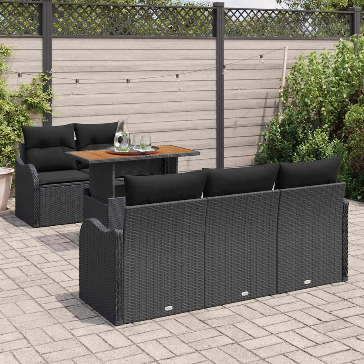 Garten-Terrassenset mit schwarzen Kissen, einem Tisch und einer Holzplatte. Die Szene umfasst einen Zaun, Pflanzen und eine Ziegelterrasse.