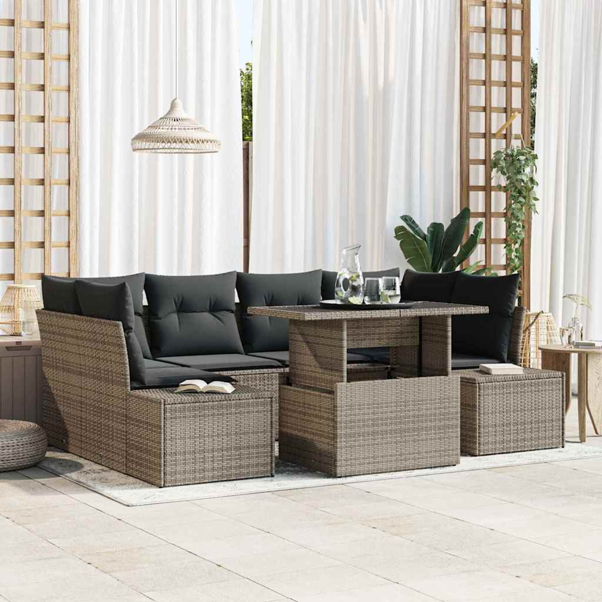 Gartenmöbel-Set aus Rattan mit grauen Kissen, einem Tisch mit Gläsern und einer Kanne. Weiße Vorhänge im Hintergrund.