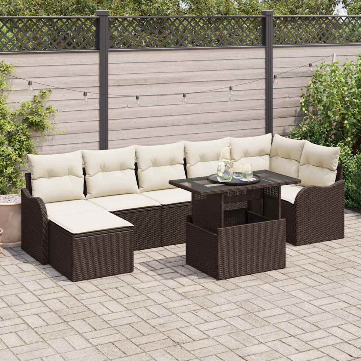 Terrassenset mit braunen Korbmöbeln und cremefarbenen Kissen. Ein Couchtisch steht davor. Holzzaun und grüne Pflanzen im Hintergrund.