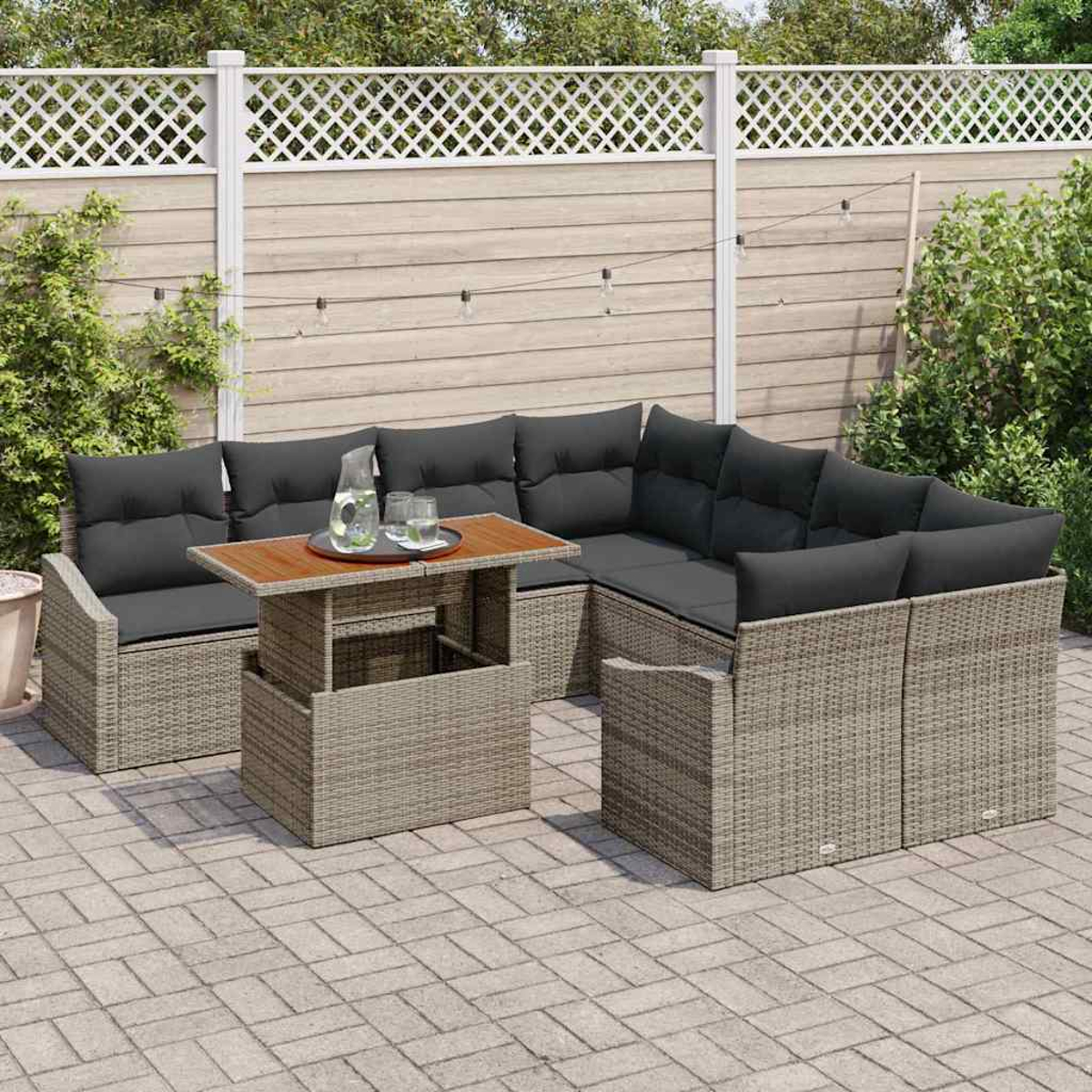 Outdoor-Sitzbereich mit einem Korbmöbel-Sofa, einem Couchtisch und Kissen. Im Hintergrund ein Zaun und Grün.