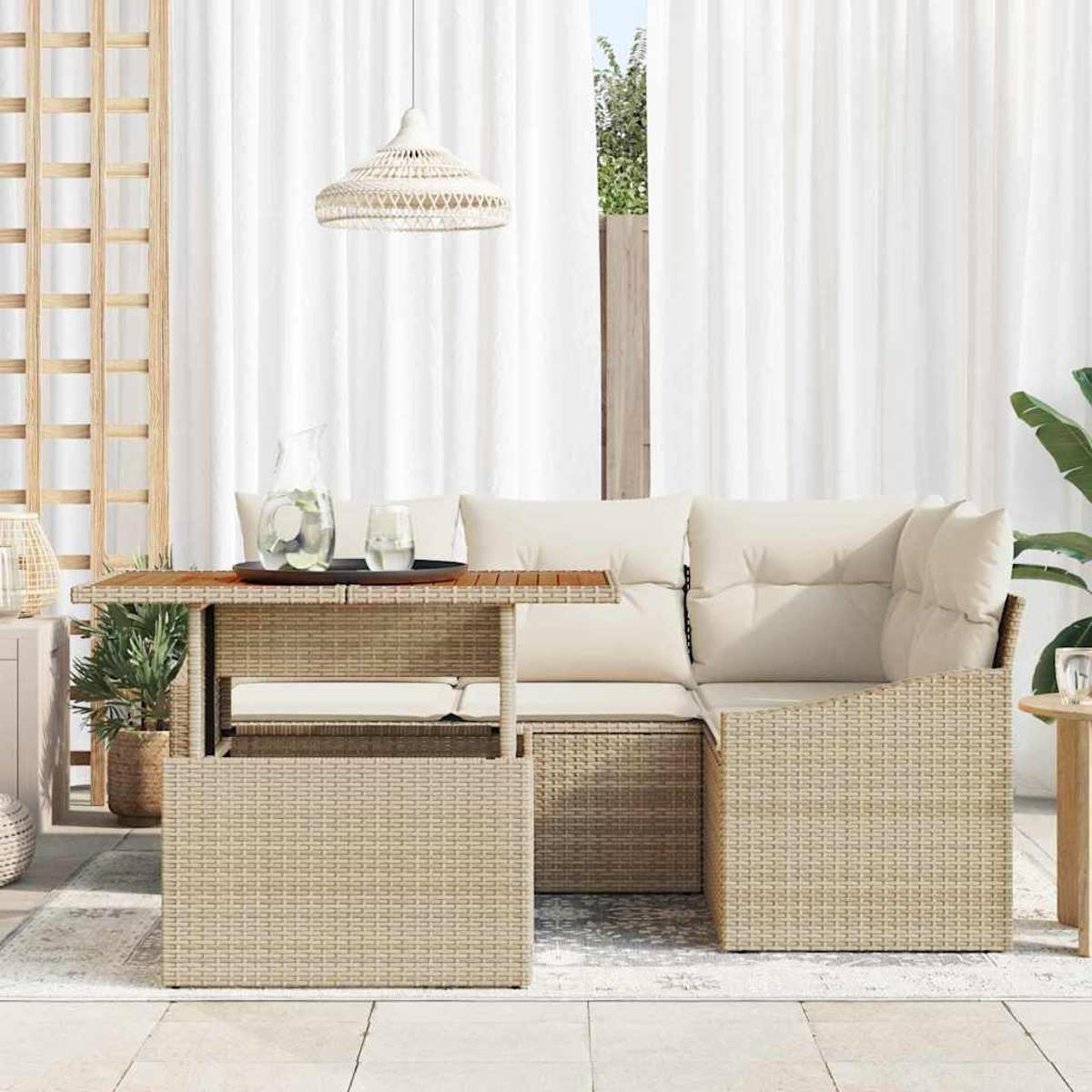 Escena al aire libre con mesa de mimbre, sofá y lámpara colgante. Bebidas en la mesa. Cortinas blancas al fondo. Plantas y sol.