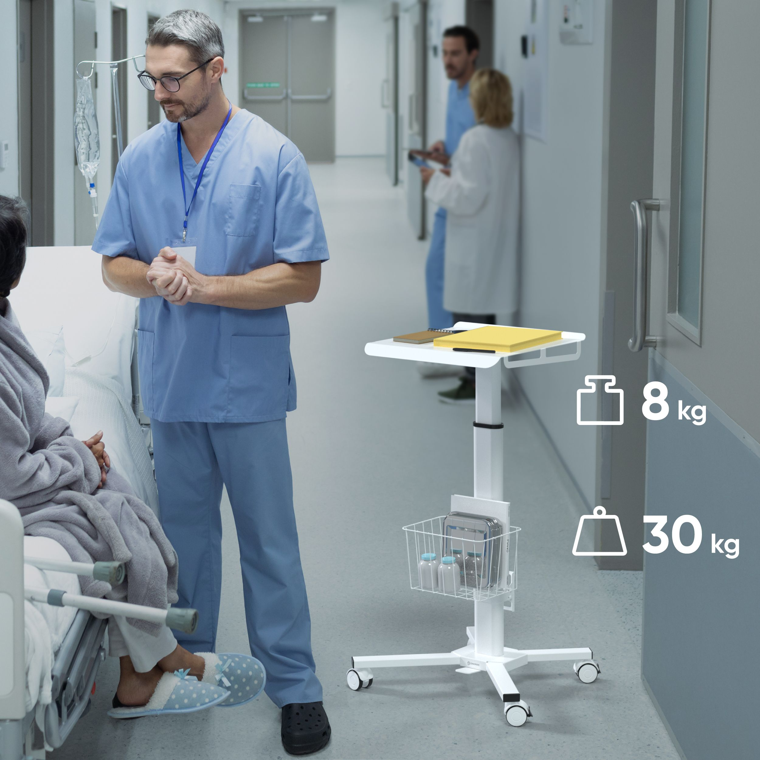Eine Krankenschwester spricht mit einem Patienten in einem Krankenhauszimmer. Ein medizinischer Wagen steht daneben. Anderes Personal ist im Flur.