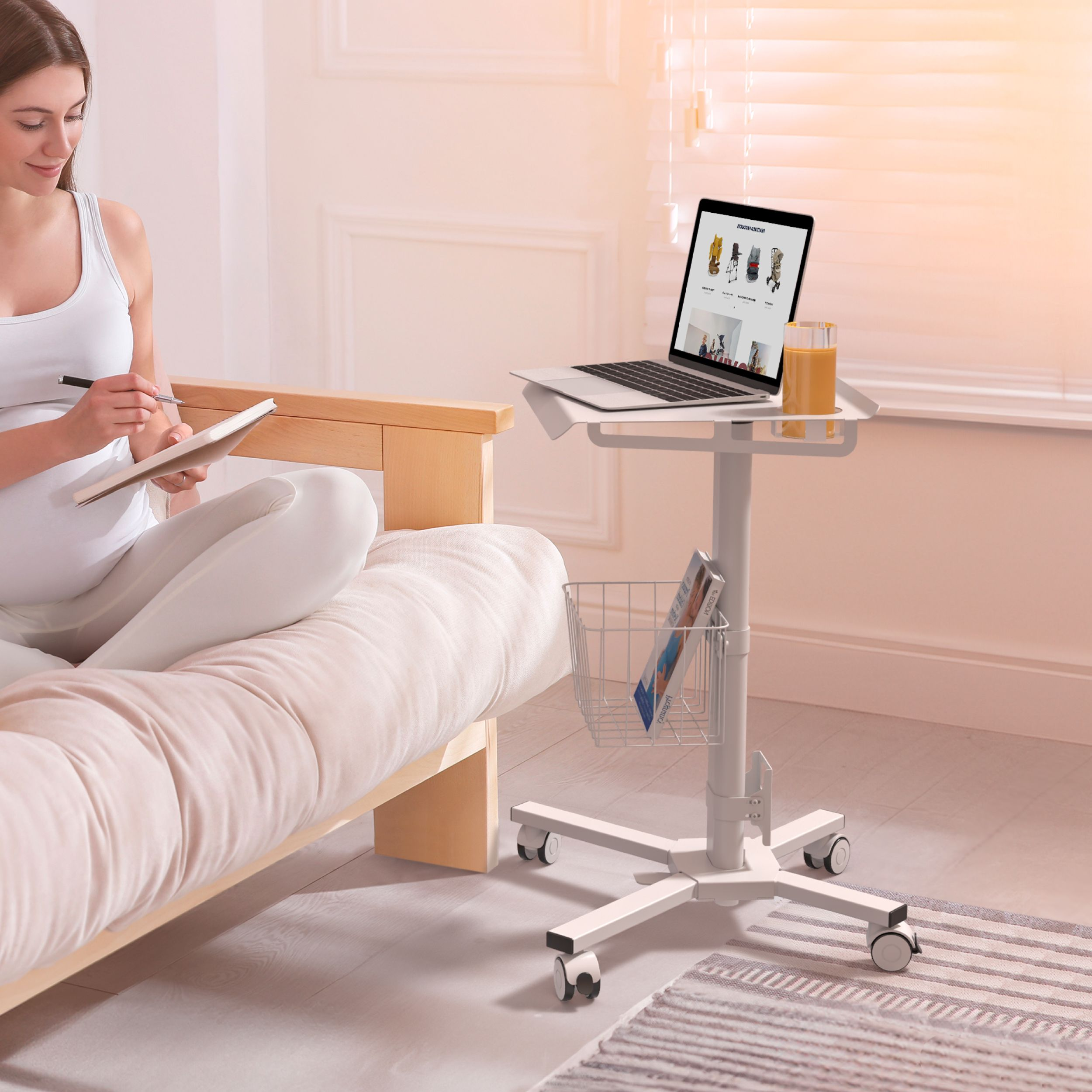 Eine Frau sitzt auf einem Bett und schreibt. Auf einem rollenden Tisch steht ein Laptop mit einer Website. Daneben steht ein Saftglas.