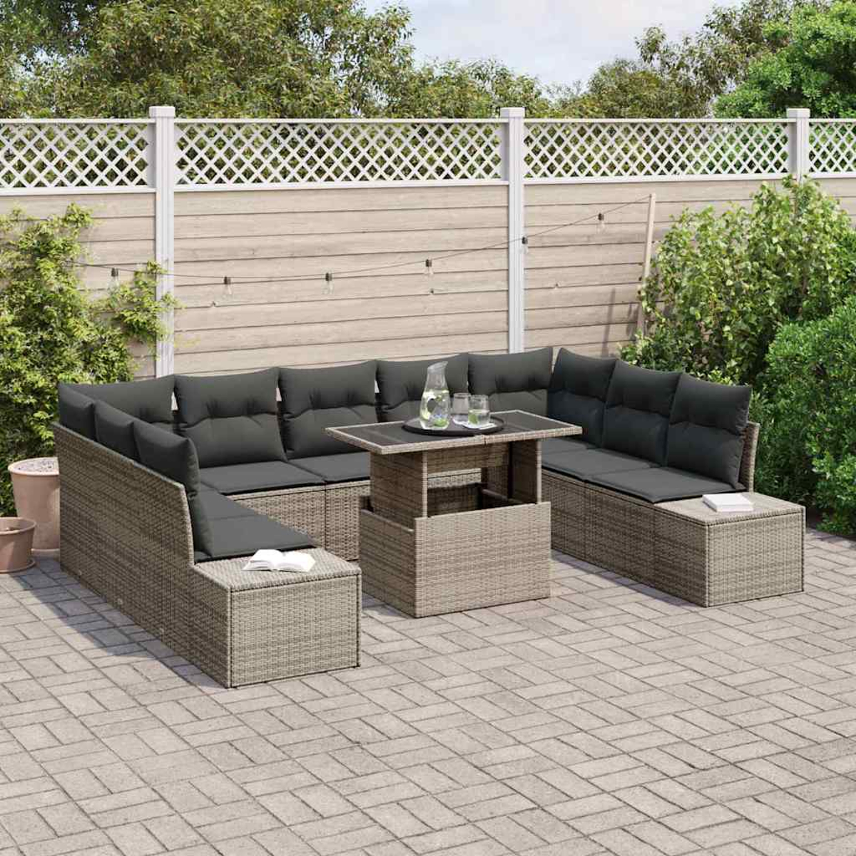 Outdoor-Ecksofa mit dunklen Kissen und einem Tisch mit Getränken auf einer Terrasse. Zaun und Grün im Hintergrund.
