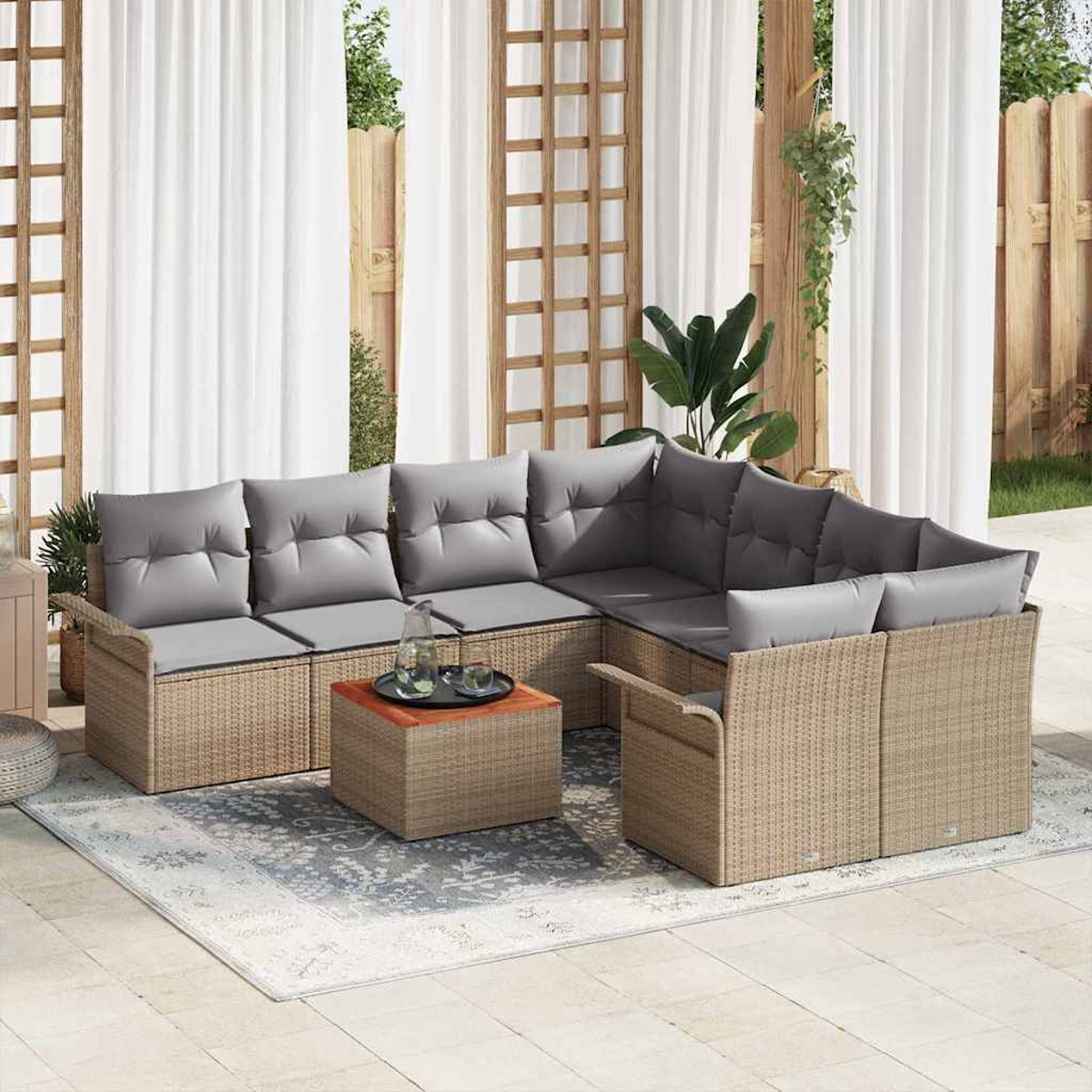 Garten-Sitzgruppe mit grauen Kissen auf einem beigen Korbgestell, einem kleinen Holztisch und einem gemusterten Teppich.