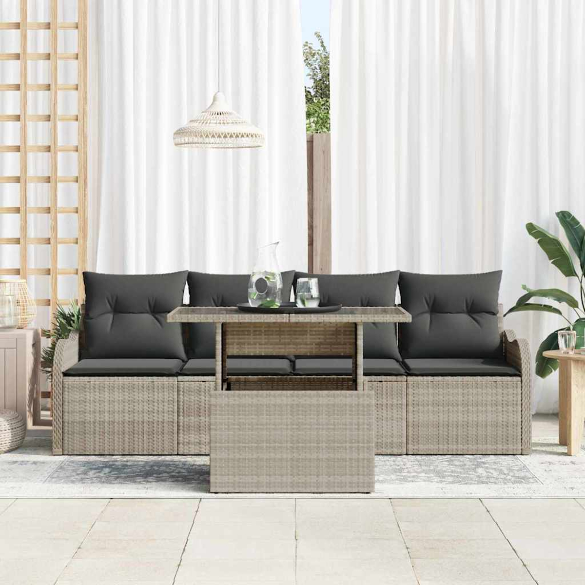 Conjunto de asientos al aire libre con sofá tejido, mesa y cojines grises. Cortinas blancas al fondo y una lámpara colgante.
