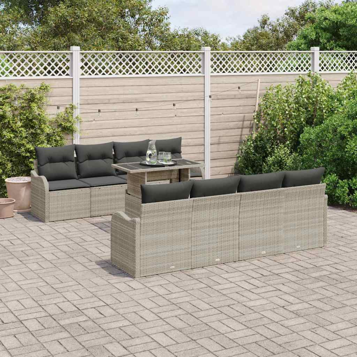 Terrassenset im Freien mit grauen Kissen, Tisch und Zaun in einem Hinterhof. Ziegelboden, Grün im Hintergrund.