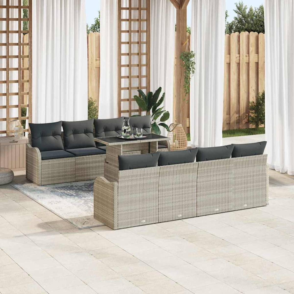 Außenbereich mit Rattansofas, Kissen, Tisch und Vorhängen. Ein Holzzaun, Pflanzen und ein Teppich vervollständigen die Szene.
