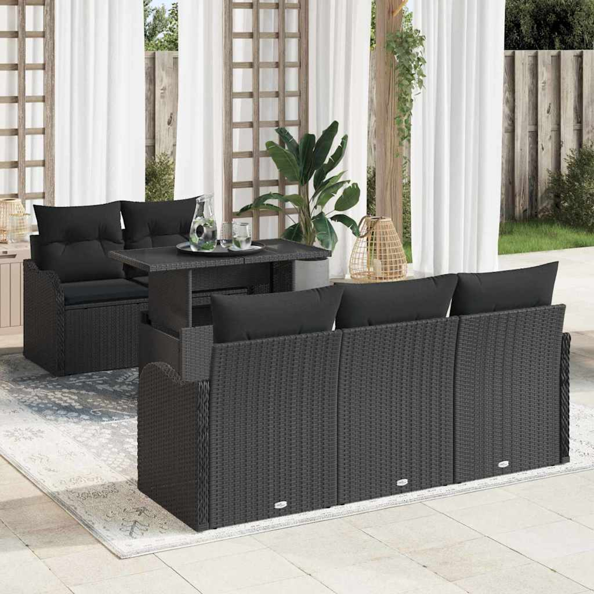 Terrassenmöbel-Set im Freien mit dunklen Korbmöbeln, schwarzen Kissen und einem Tisch. Weiße Vorhänge und eine Pflanze im Hintergrund.