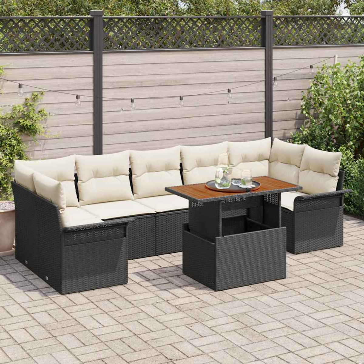 Gartenmöbel-Set. Dunkles Korbssofa mit cremefarbenen Kissen, Couchtisch und Holzzaun im Hintergrund.