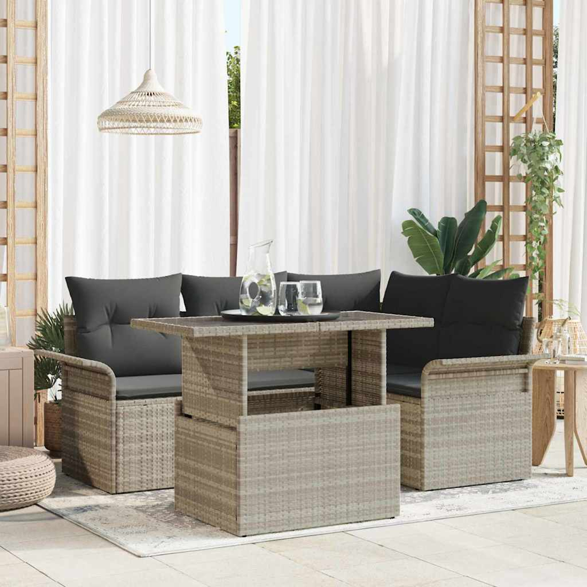 Un juego de asientos beige para exteriores con cojines grises se encuentra sobre una alfombra. Una mesa tiene vasos y una jarra. Cortinas blancas en el fondo.