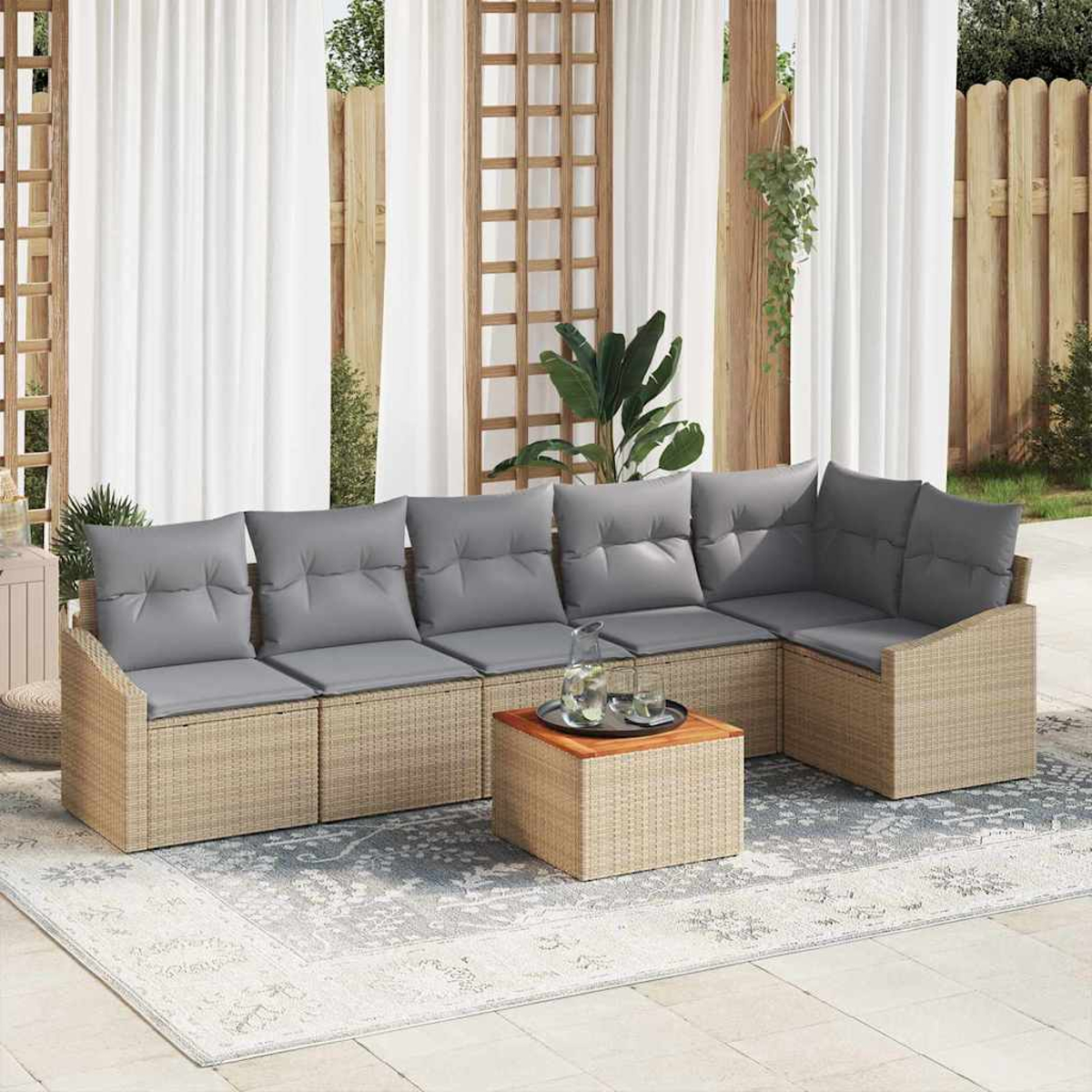 Ein Ecksofa im Freien mit grauen Kissen und einem Holztisch steht auf einem gemusterten Teppich. Weiße Vorhänge und Holzzaun im Hintergrund.