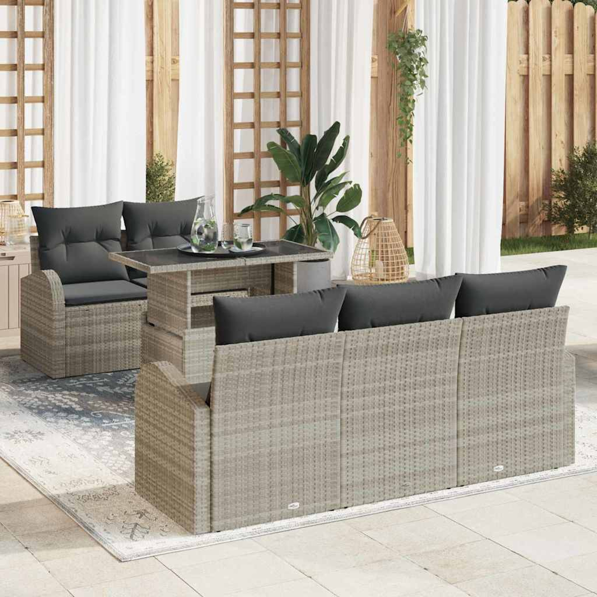 Gartenmöbel mit grauem Korbmöbel, schwarzen Kissen, einem Tisch mit Glas und Pflanzen. Weiße Vorhänge und Holz-Hintergrund.