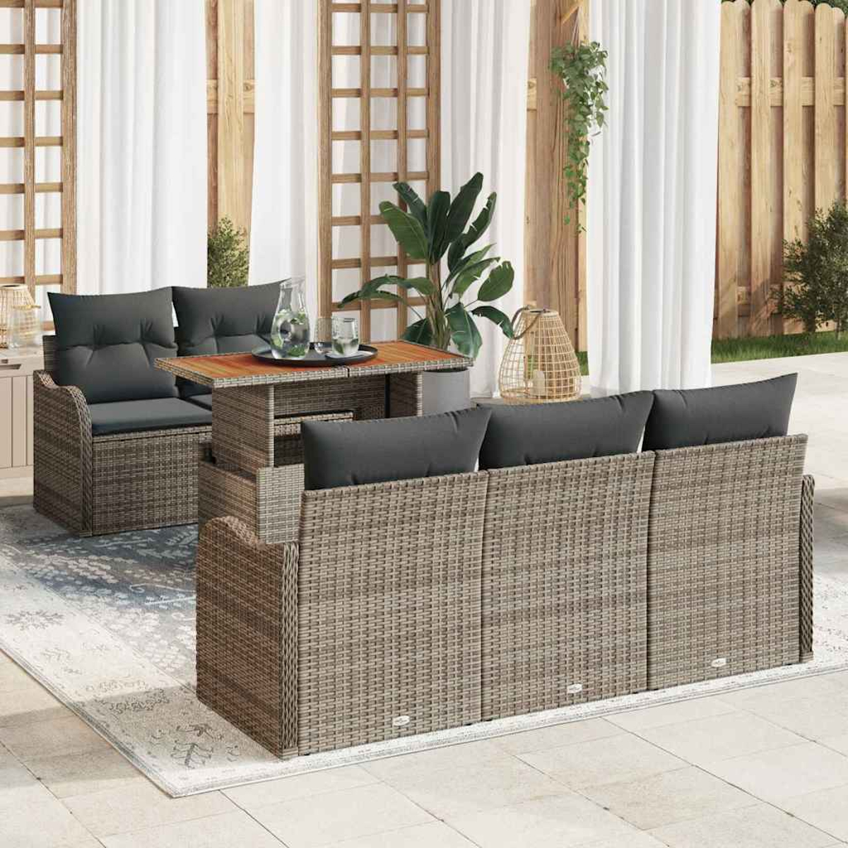 Sitzbereich im Freien mit Korbmöbeln, grauen Kissen und einem Holztisch auf einem gemusterten Teppich.