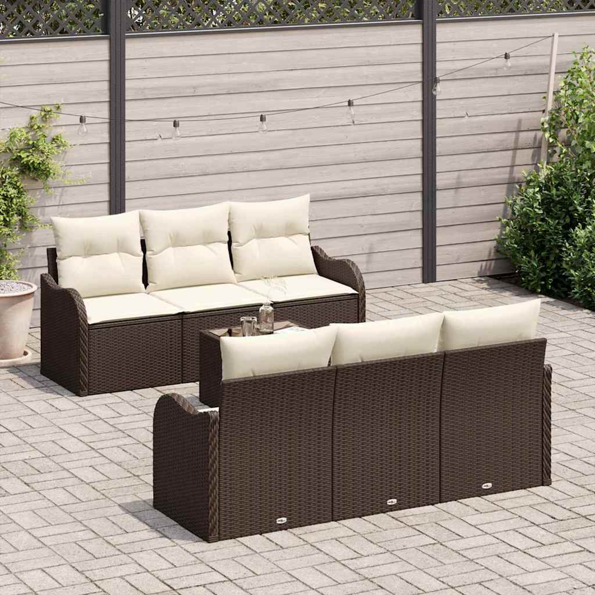 Gartenmöbel: zwei braune Korbsitzgruppen mit cremefarbenen Kissen. Ein kleiner Tisch mit Gläsern steht dazwischen. Dahinter ein Holzzaun.
