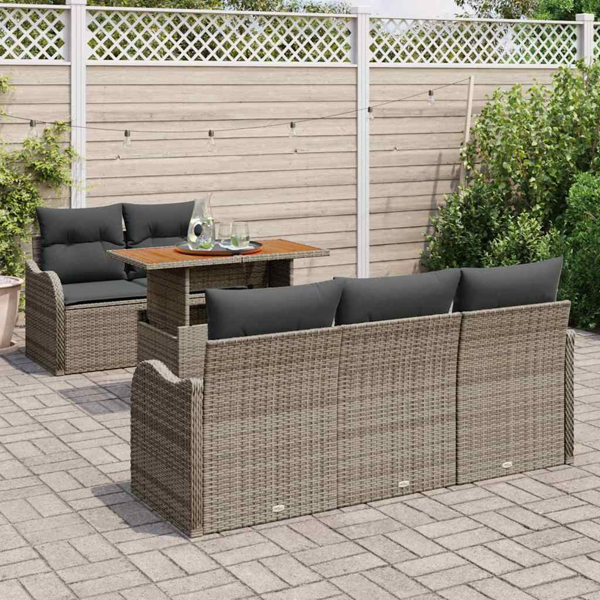 Garten-Set mit grauen Kissen auf Korbmöbeln. Ein Tisch mit Getränken steht zwischen Sofa und Stuhl. Holzzaun im Hintergrund.