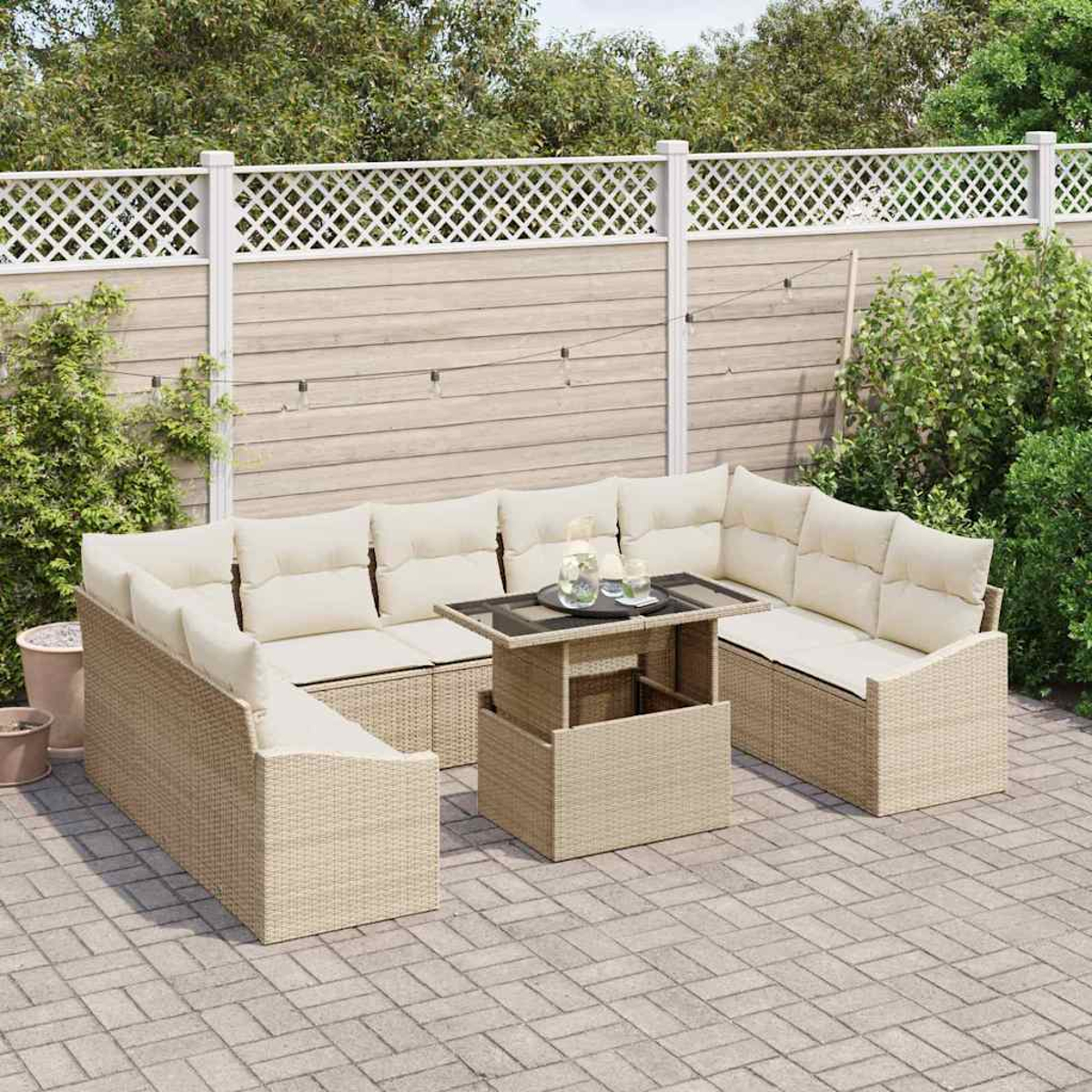 Beiges Outdoor-Ecksofa aus Korbgeflecht mit cremefarbenen Kissen und einem Tisch auf einer Backstein-Terrasse, mit Zaun und Grün im Hintergrund.