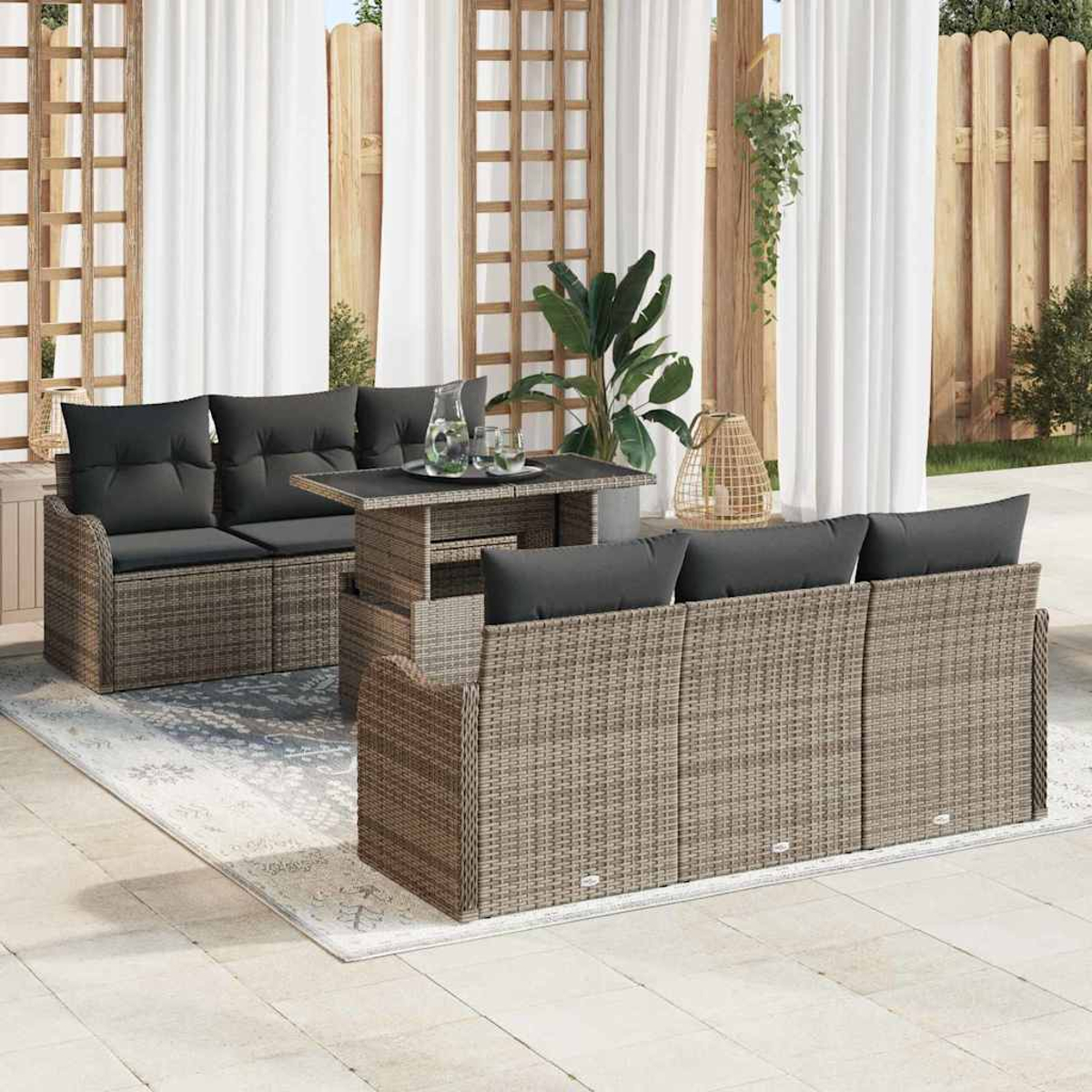Juego de muebles de ratán para exteriores: sofá, sofá de dos plazas y mesa con cojines negros. Fondo con cortinas blancas y plantas.