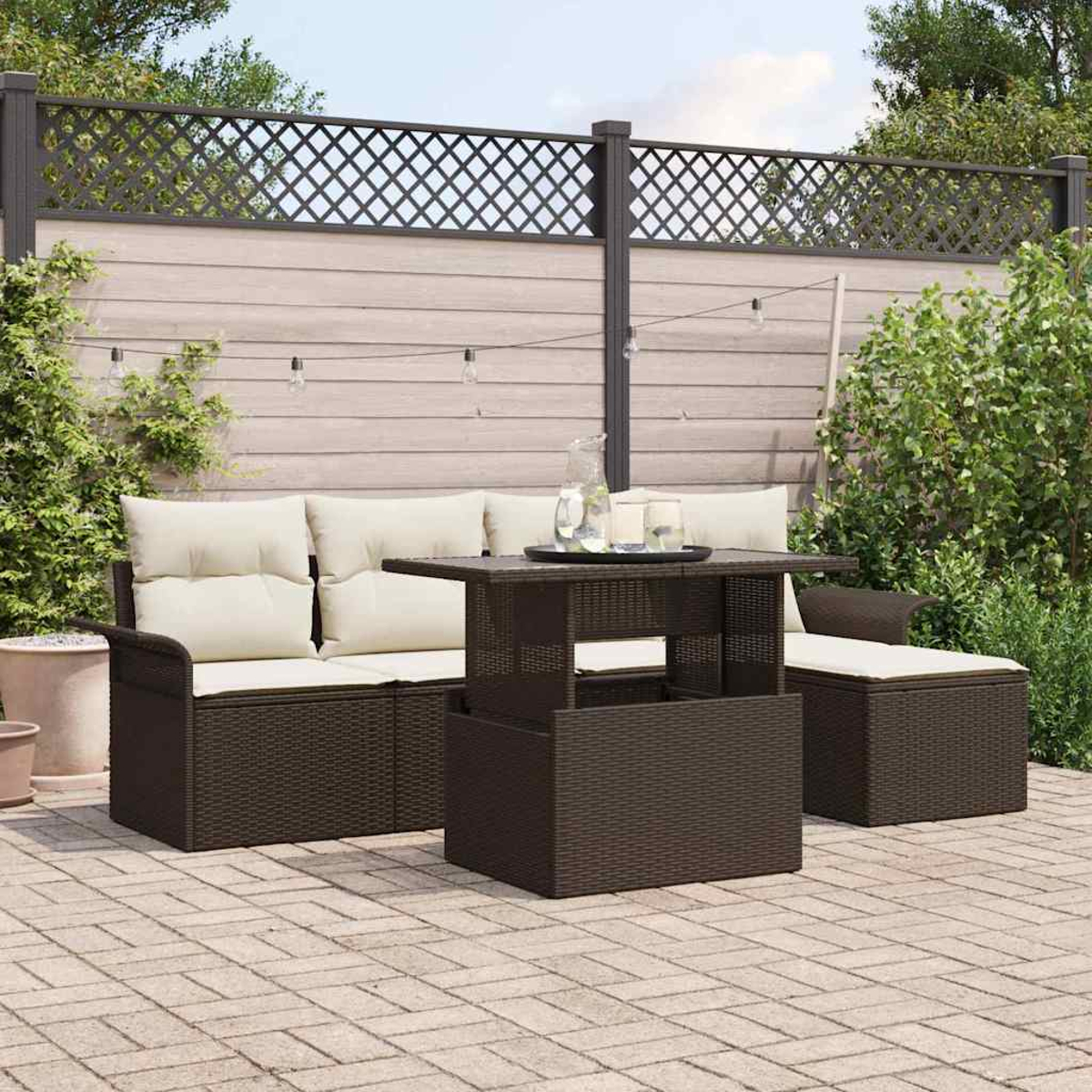 Szene im Freien mit einem braunen Korbmöbel-Set. Beige Kissen, ein Zaun mit Lichtern und eine Backstein-Terrasse sind sichtbar.