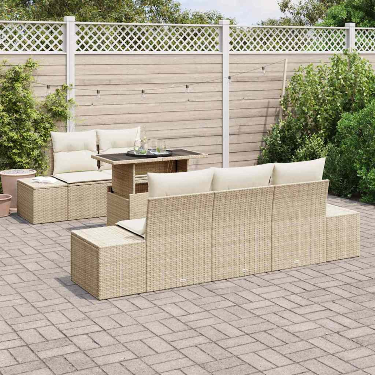 Outdoor-Korbsitzgruppe mit cremefarbenen Kissen und einem passenden Tisch auf einer Backstein-Terrasse. Im Hintergrund ein Holzzaun und Grün.