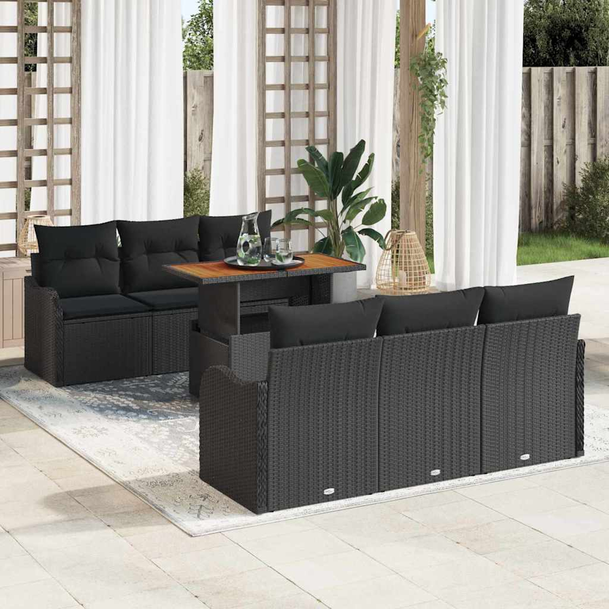 Terrassenmöbel-Set mit schwarzem Korbmöbel, Kissen und Holztisch. Weiße Vorhänge, Pflanzen und ein Teppich sind sichtbar.
