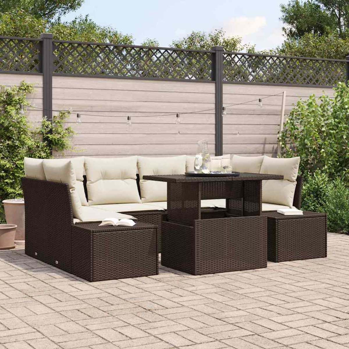 Rattanset für den Außenbereich. Dunkelbraunes Sofa mit cremefarbenen Kissen, Tisch und zwei Ottomanen auf einer Ziegelterrasse, mit Holzzaun.