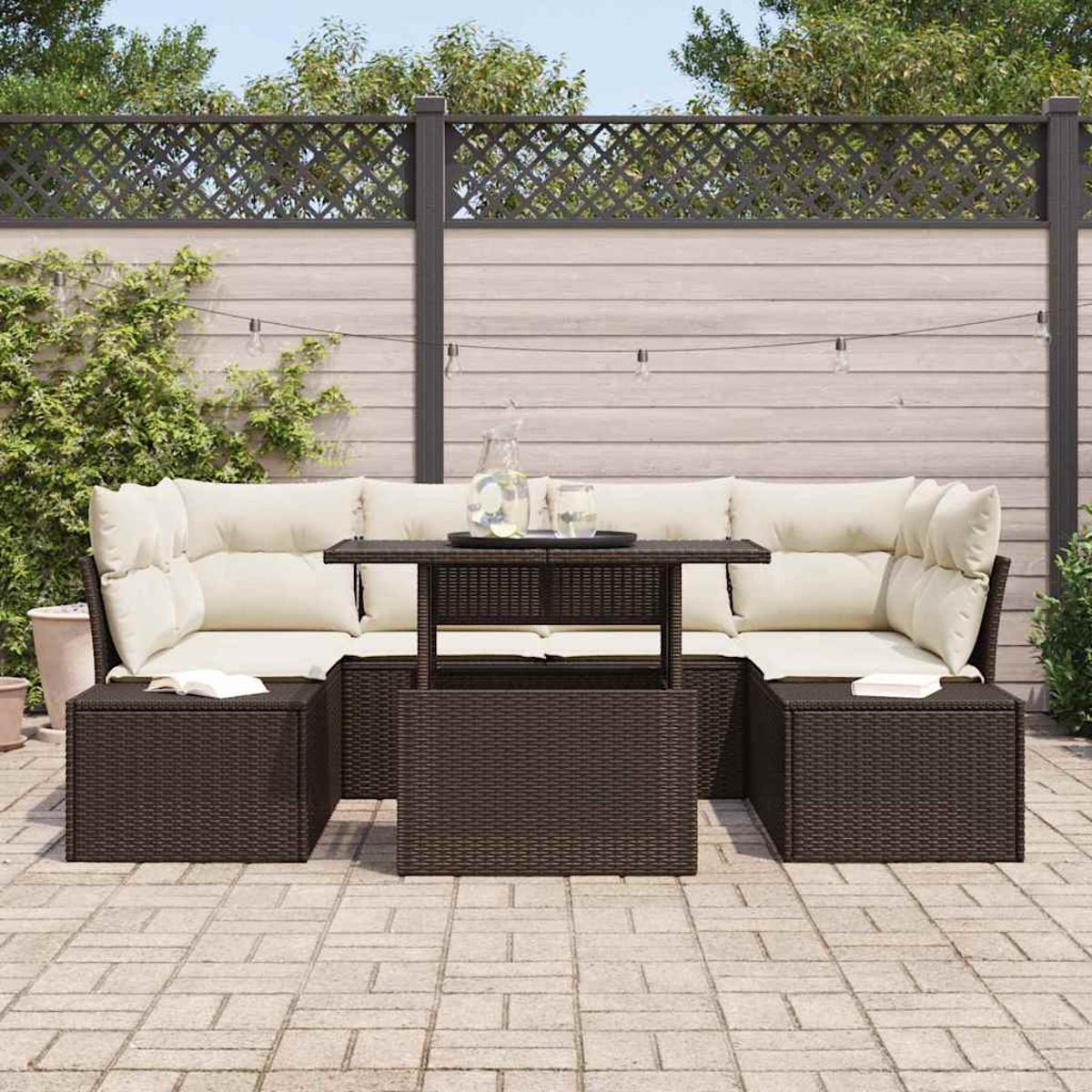 Gartenmöbelset. Enthält Korbsessel, Ottomanen, Couchtisch und Kissen. Im Hintergrund sind Zaun und Pflanzen.