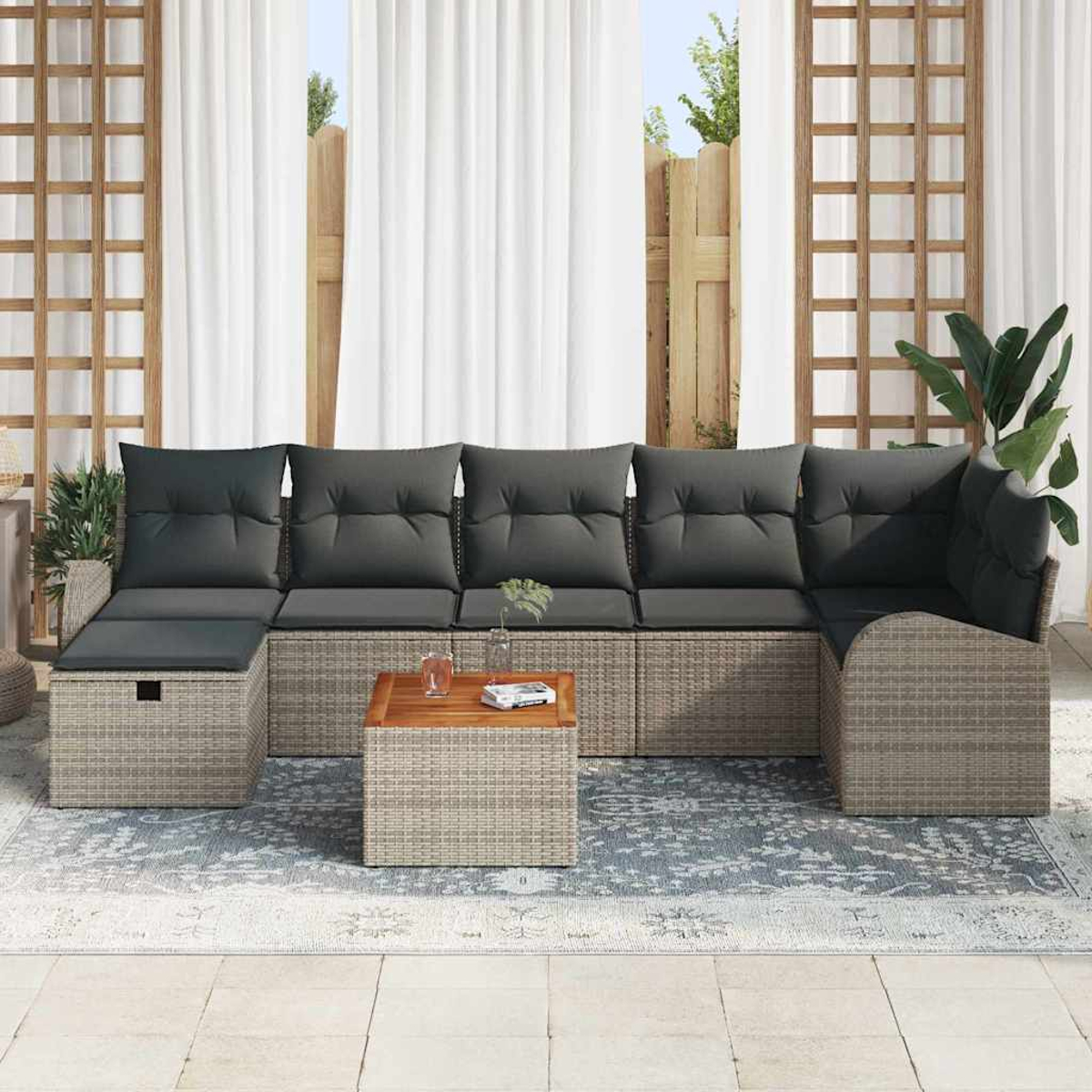 Outdoor-Ecksofa mit grauen Kissen und einem hölzernen Beistelltisch auf einem gemusterten Teppich. Weiße Vorhänge und Pflanzen sind im Hintergrund.