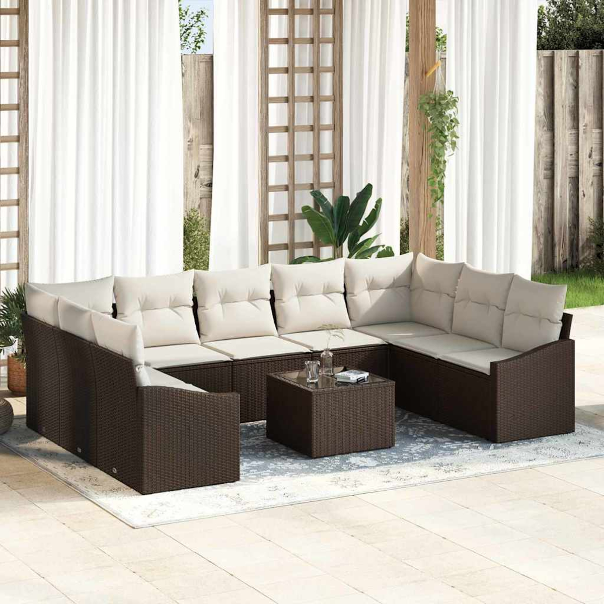 Garten-Sitzgruppe mit braunen Korbmöbeln, beigen Kissen und einem Couchtisch mit Glasplatte, auf einem Teppich, mit weißen Vorhängen.