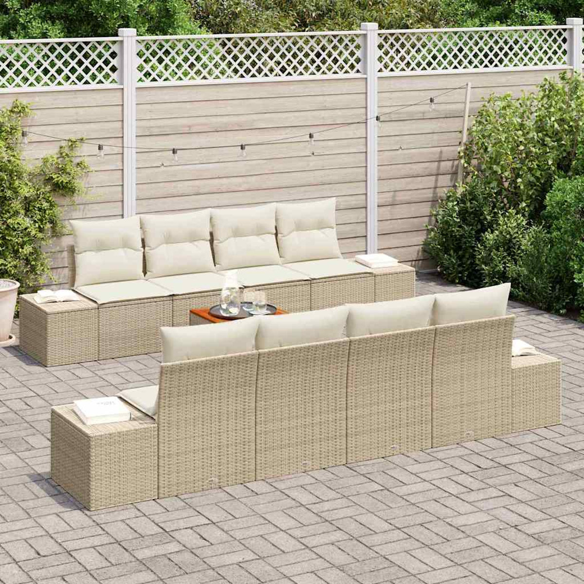 Outdoor-Sitzarrangement. Beige Korbsessel mit cremefarbenen Kissen auf einer Ziegelterrasse. Ein Holztisch mit Getränken. Weißer Zaun im Hintergrund.