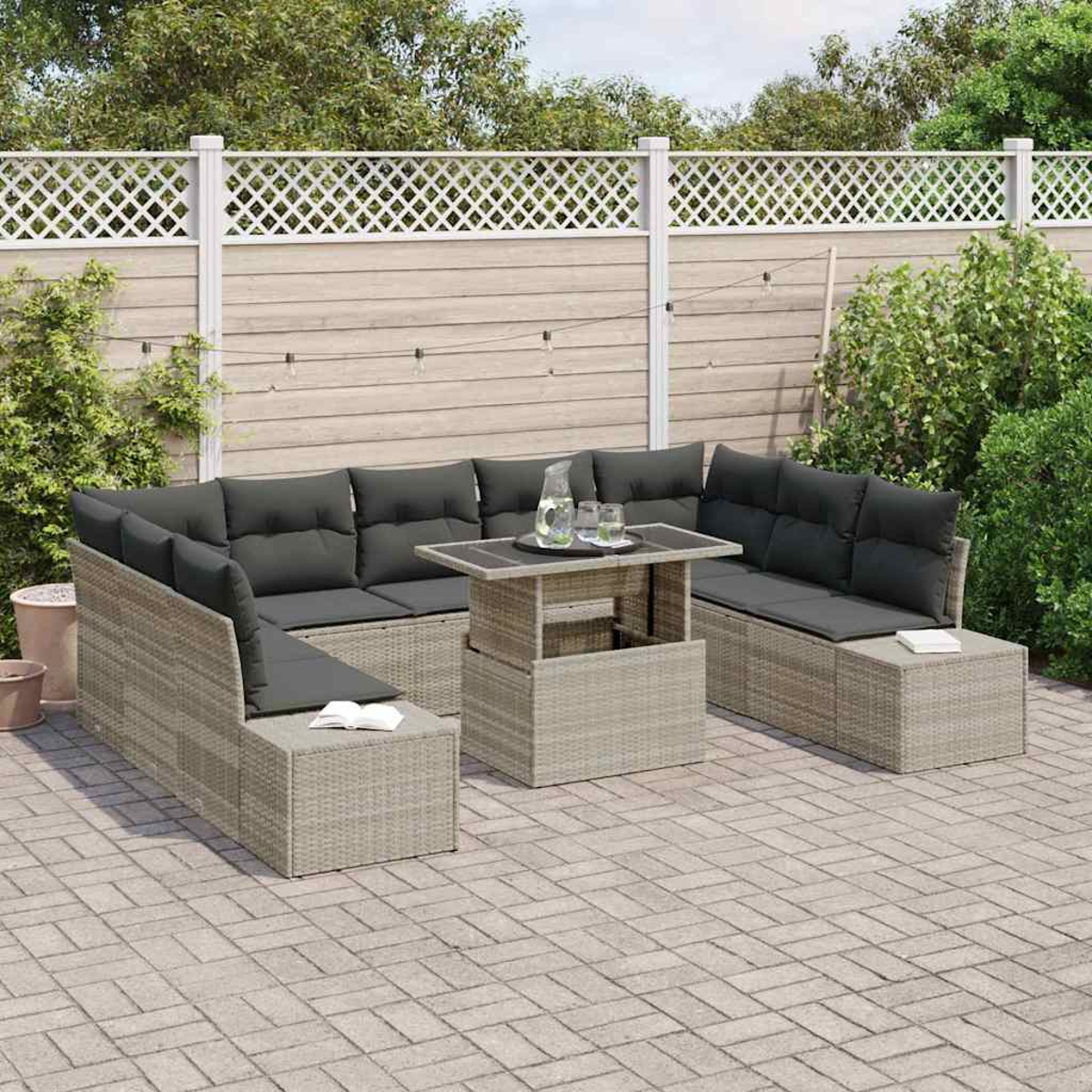 Garten-Terrassenset mit grauen Kissen und einem Tisch. Beige Korbmöbel auf einer gepflasterten Terrasse. Weißer Gitterzaun im Hintergrund.