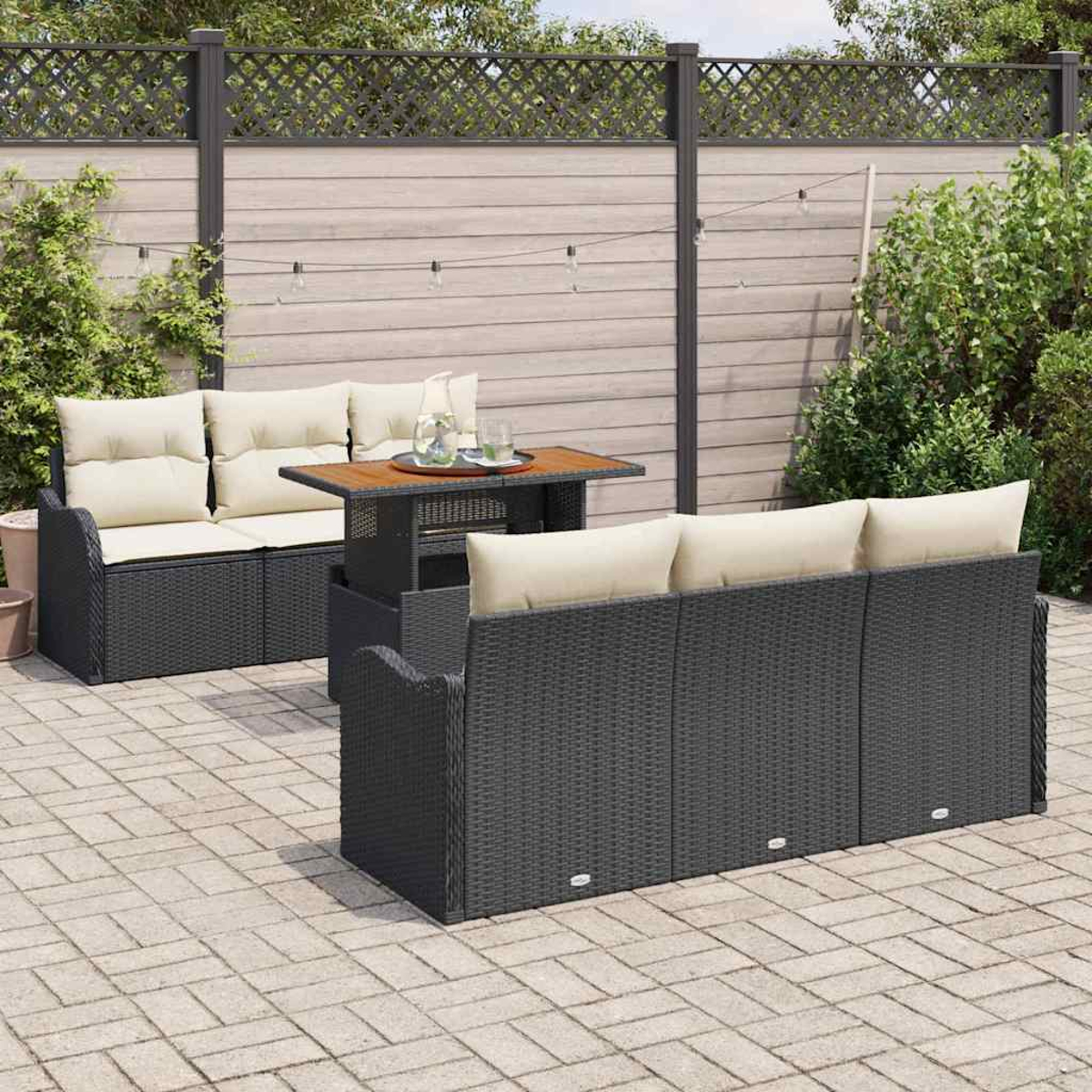 Terrassenmöbel-Set mit schwarzen Webmöbeln, beigen Kissen und einem Holztisch vor einem Holzzaun und Grün.