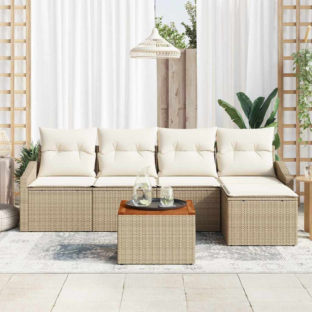 Szene im Freien mit einem Rattansofa, Kissen und Couchtisch. Kanne und Gläser stehen auf dem Tisch. Hintergrund umfasst Vorhänge und Pflanzen.